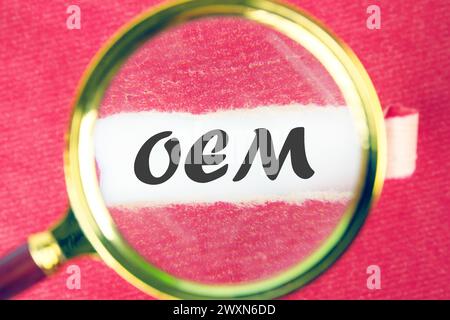 OEM original equipment manufacturer concept. Text through a magnifying glass under a torn piece of paper Stock Photo