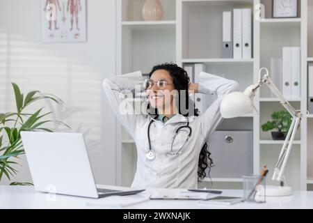 A Latino female doctor takes a moment to relax at her desk in a well-lit, modern medical office, exuding a sense of calm and professionalism. Stock Photo