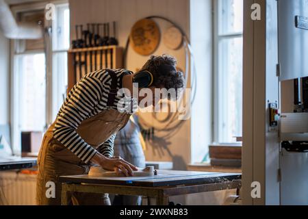 Man carpenter wear protective noise-cancelling headphones turning wood on lathe working in joinery Stock Photo
