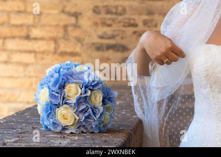 a bride's hand gently touches her veil near the bouquet of blue hydrangeas and white roses, signifying matrimonial joy Stock Photo