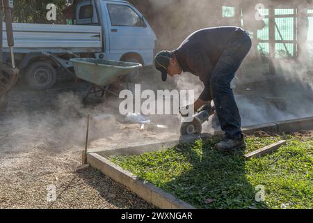 A worker builds a curb using various tools including an angle grinder Stock Photo