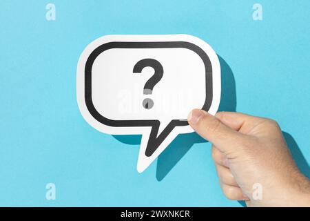 Hand holding a question mark on speech bubble on blue background. Doubt, confusion, uncertainty concept Stock Photo