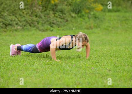 Young woman doing pushups in a meadow Stock Photo