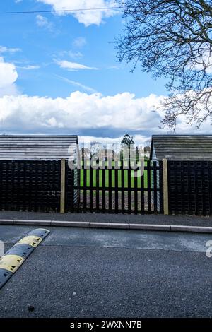 Leatherhead Surrey, UK, April 01 2024, Two Black Painted Wooden Sheds With Metal Fence And Tree In School Playing Fields With No People Stock Photo