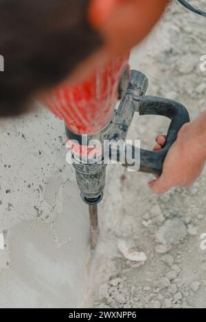 A man using a hand-held drill for concrete work on a sidewalk Stock Photo