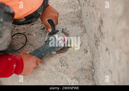 A construction worker in an orange shirt using a rotary tool on a cement wall Stock Photo