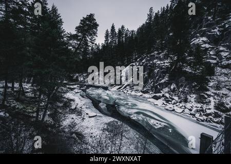 Snow-covered trees and rocks by a frozen stream in a winter landscape Stock Photo