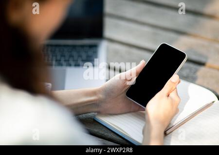 Close-up of a woman's hands holding a smartphone with a blank screen above an open notebook Stock Photo