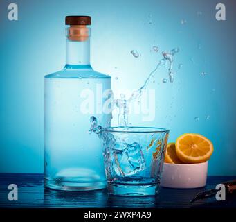 Drinks bottle and glass with ice cube and alcohol splashing out of the glass. Stock Photo
