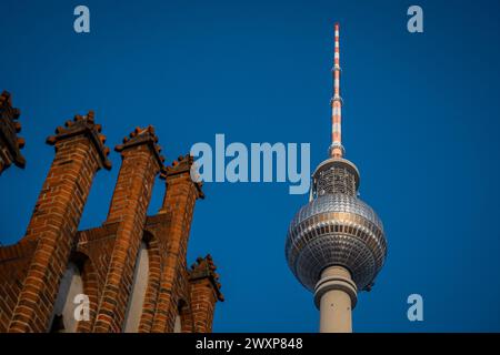 Tv tower in Berlin, on Alexanderplatz square on a clear spring day. Prominent tall building in Berlin, Germany. Looking from side behind red bricks of Stock Photo