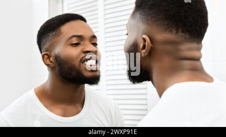 Man brushing teeth looking at bathroom mirror Stock Photo