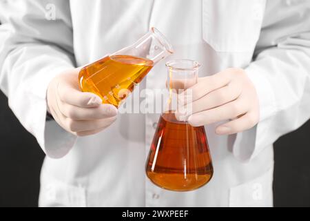 Woman pouring yellow crude oil into flask on dark background, closeup Stock Photo