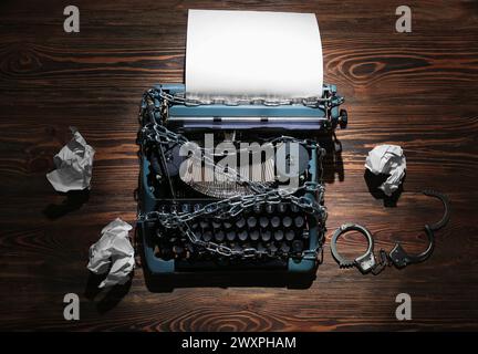 Vintage typewriter with chains, handcuffs and crumpled paper on wooden background. Printing ban concept Stock Photo