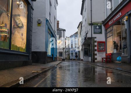 View along a virtually empty Fore Street on a rainy spring day, with grey sky, and rain falling in the puddles. Stock Photo