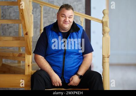 Problems with excess weight after 40 years, tall Caucasian man, 47 years old, sits on steps of stairs leading to second floor. Stock Photo