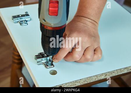 Furniture assembler installs adjustable door hinges into particle board of door cabinet from flat pack. Stock Photo