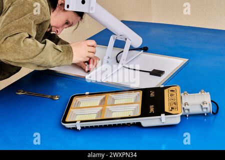 Assembling stand alone solar street light, an electrician attaches solar module and LED luminary to light arm or mounting bracket. Stock Photo