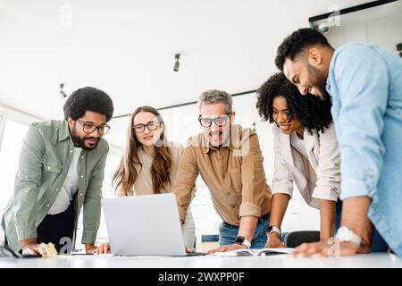 A group of diverse professionals is standing around a laptop, highlighting a moment of team collaboration and digital strategy planning, solving project tasks, or analyzing the result Stock Photo