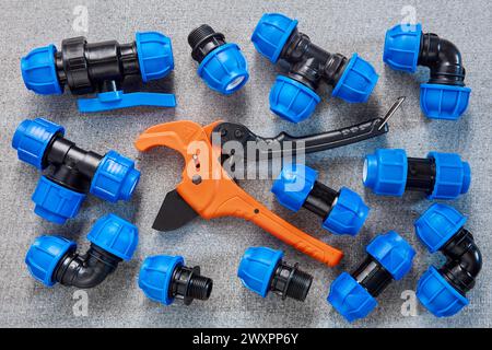 A collection of blue polyethylene pipe fittings is neatly arranged alongside an orange PVC pipe cutter, possibly during a plumbing project. Stock Photo