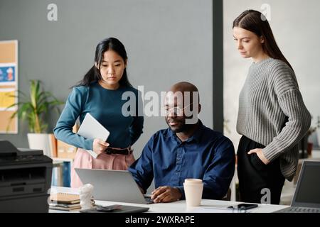 Medium long shot of three ethnically diverse millennial managers working together on business strategy in modern office Stock Photo