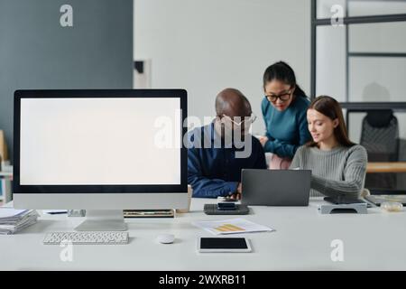 Selective focus shot of three ethnically diverse managers working on project in modern office. Computer monitor with blank screen standing on desk Stock Photo