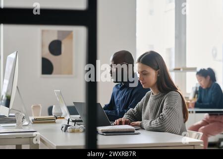 Group of three young ethnically diverse people working on laptops at workplace in modern office, copy space Stock Photo