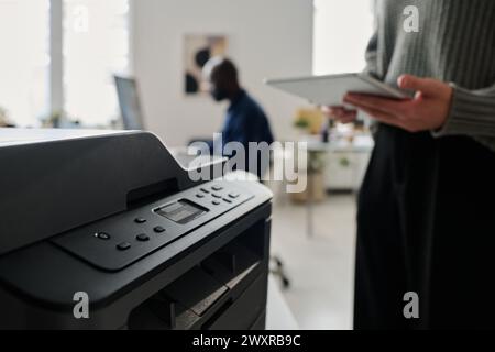 Selective focus of unrecognizable young woman holding digital tablet while using printer in office, copy space Stock Photo