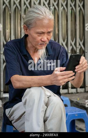 Elderly man looking at his mobile phone in the Old Quarter of Hanoi, Vietnam Stock Photo