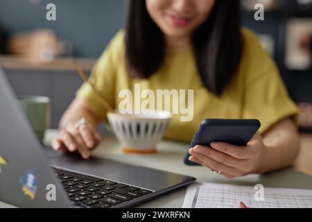Selective focus shot of young Asian woman reading message on smartphone while scrolling web page in Internet on smartphone during breakfast Stock Photo