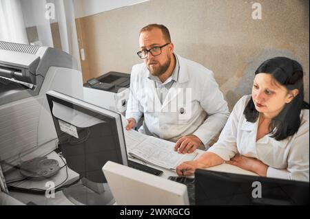 Two doctors working at computers. Specialists wearing white robes, making MRI, consulting, examining results. Concept of modern diagnostics. Stock Photo