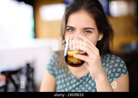 Happy woman drinking soda looking at you sitting in a bar interior Stock Photo