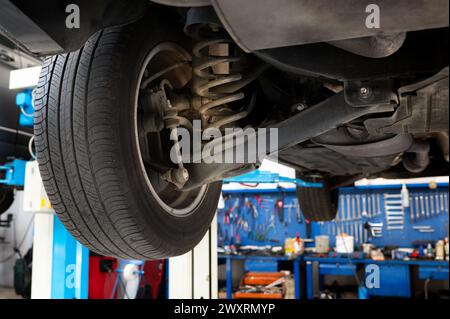 Bottom view of lifted car wheel with spring and shock absorber for repair in garage against neatly arranged various mechanic tools and instruments in Stock Photo