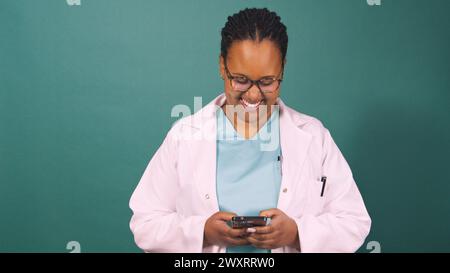 Young Black female doctor works on cellphone, smiling and typing Stock Photo