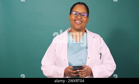 Young Black female doctor works on cellphone, smiling to camera Stock Photo
