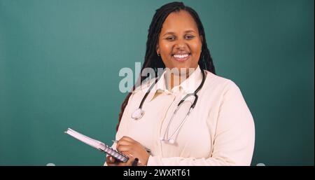 Young Black female doctor making notes on writing pad, smiling Stock Photo