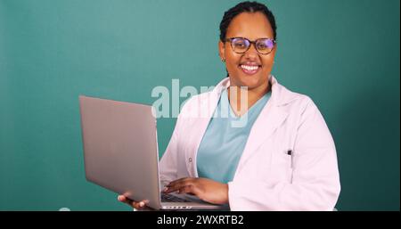 Young Black female doctor works on laptop, smiles at the camera Stock Photo