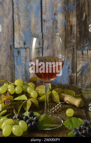 Glass of red wine with green grapes and corkscrew on wooden background. Stock Photo