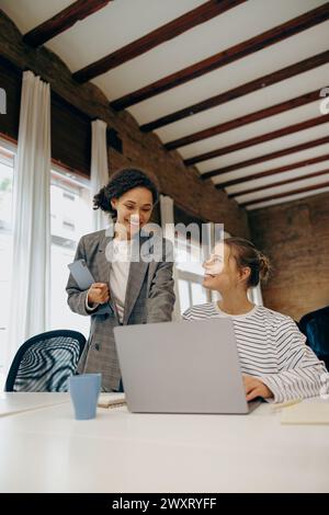 Two smiling busy female colleagues working on project together and use laptop sitting in office Stock Photo