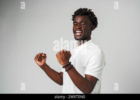Smiling Young Man In White Polo Shirt Celebrating With Raised Fists Indoor Stock Photo
