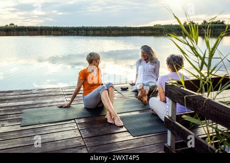 Group of senior woman sitting on yoga mats talking after exercise. Stock Photo