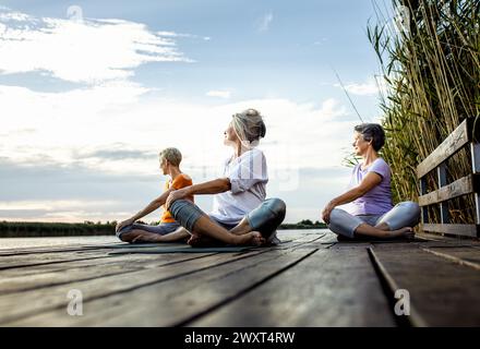 Group of senior woman doing yoga exercises by the lake. Stock Photo