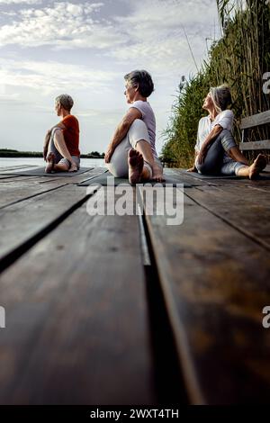 Group of senior woman doing yoga exercises by the lake. Stock Photo