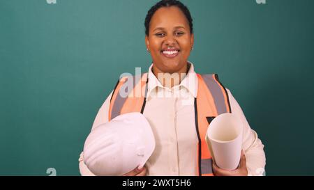 Young Black construction worker smiling holding hard hat, working on site Stock Photo