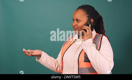 Beautiful young Black female construction worker talking on cellphone, architect Stock Photo