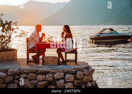 Couple in love drinking wine on romantic dinner at sunset on the beach. Stock Photo