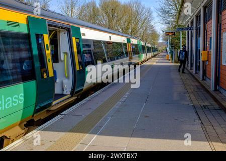 A Southern Railway train in green and yellow livery stands with its doors open at almost empty station platform Stock Photo