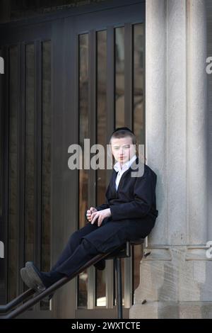 During recess at his yeshiva, an orthodox Jewish student is lost in thought while taking an impromptu seat on a stair bannister. In Brooklyn, NY Stock Photo
