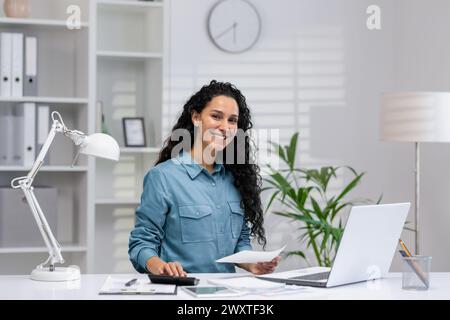 Portrait of a smiling Hispanic woman working in her home office, demonstrating professionalism and confidence. Stock Photo