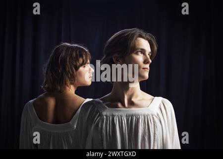 Two young and handsome men in draped white blouses, standing back-to-back and looking to one side. Stock Photo