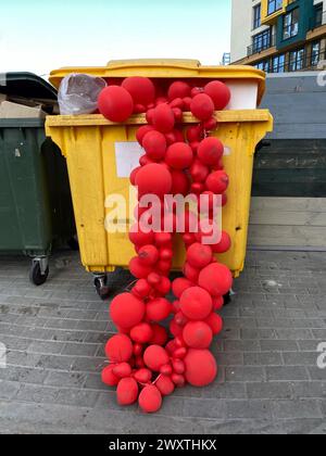 Red balloon garlands in a dumpster, selective focus. Discarded used decoration. Concept of the melancholy after holiday party Stock Photo